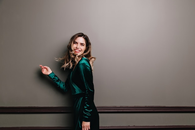 Free photo wonderful girl in green velvet dress enjoying photoshoot. enthusiastic young woman with wavy brown hair smiling