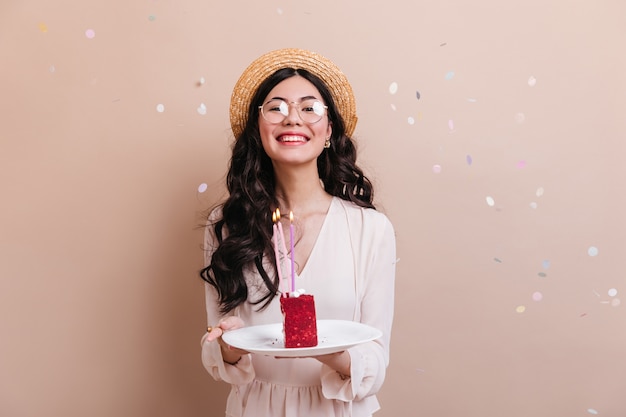 Meravigliosa donna giapponese con i capelli ricci tenendo la torta. vista frontale della donna cinese in bicchieri per celebrare il compleanno.