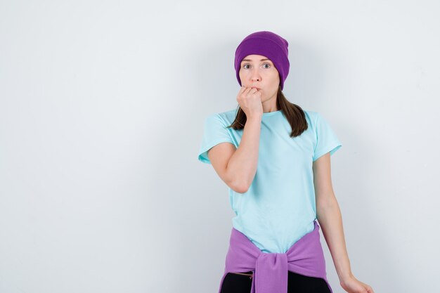 Wonderful lady in blouse, beanie keeping fist on chin and looking scared , front view.