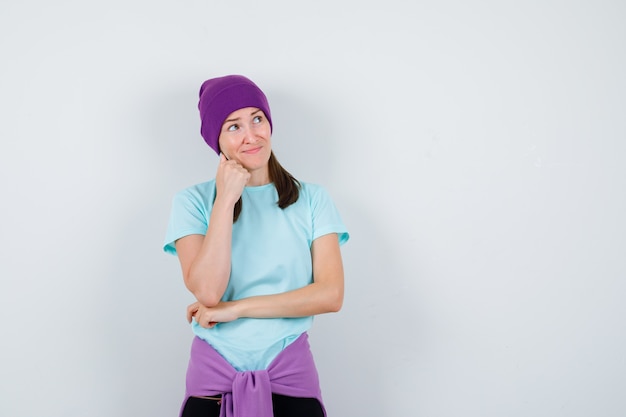 Wonderful lady in blouse, beanie keeping hand on chin and looking confident , front view.