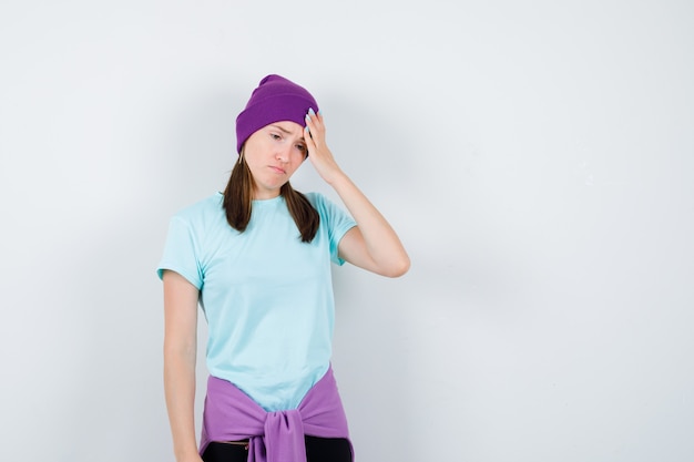 Wonderful lady in blouse, beanie keeping hand on head and looking upset , front view.