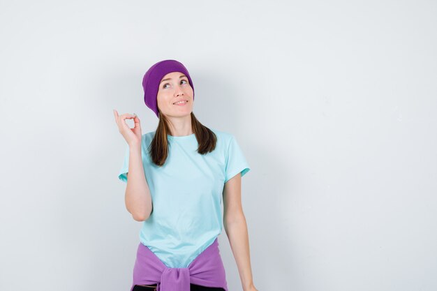 Wonderful lady in blouse, beanie pointing up and looking interested , front view.