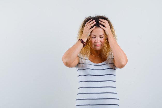 Wonderful lady holding hands on head in striped t-shirt and looking depressed , front view.