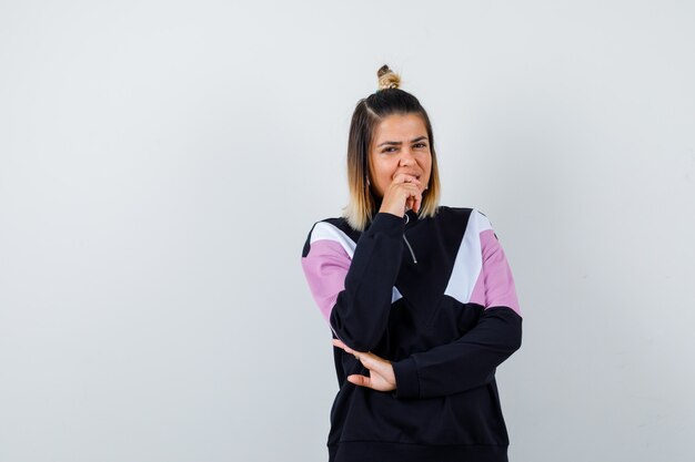 Wonderful lady keeping hand on chin in sweatshirt and looking cheerful