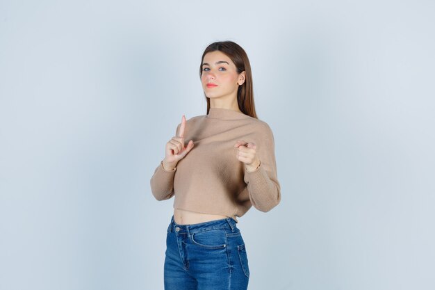 Wonderful lady pointing at front in sweater, jeans and looking confident , front view.