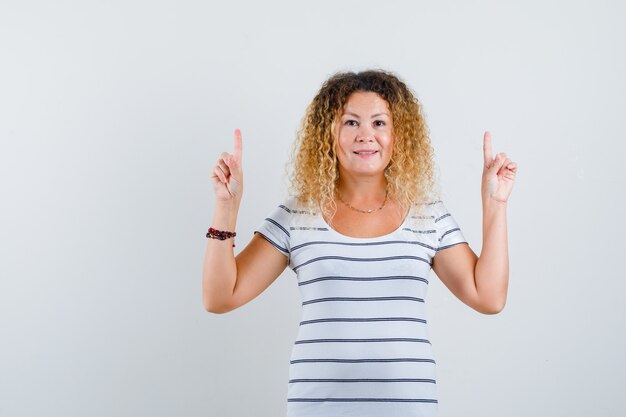 Wonderful lady pointing up in striped t-shirt and looking cheerful , front view.