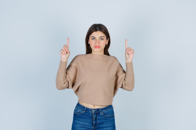 Wonderful lady pointing up in sweater, jeans and looking displeased. front view.