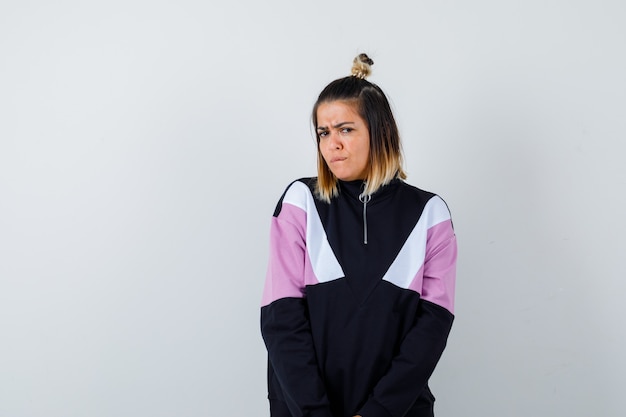 Wonderful lady posing while standing, looking at camera in sweatshirt and looking displeased