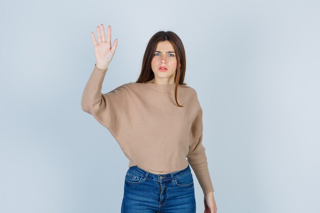 Wonderful lady showing no gesture in sweater, jeans and looking displeased , front view.