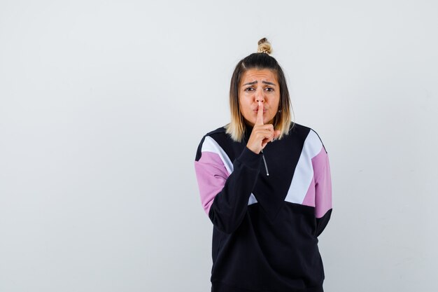 Wonderful lady showing silence gesture in sweatshirt and looking serious