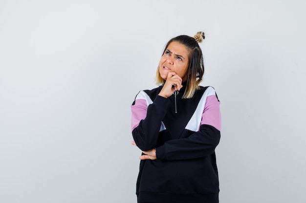 Wonderful lady in sweatshirt keeping hand on chin and looking thoughtful