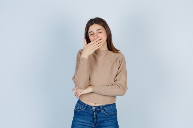 Wonderful lady with hand on mouth while laughing in sweater, jeans and looking jovial. front view.