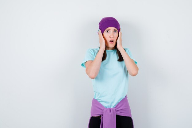 Wonderful lady with hands on head, opening mouth in blouse, beanie and looking terrified , front view.