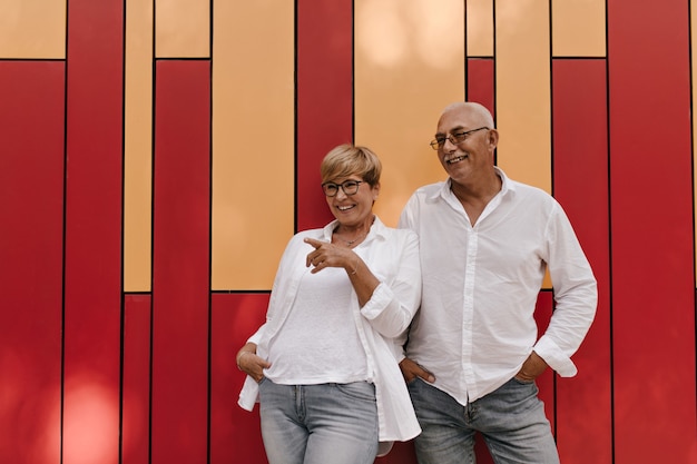 Free photo wonderful lady with short hair in light clothes and eyeglasses laughing with man with mustache in white clothes on red and orange.