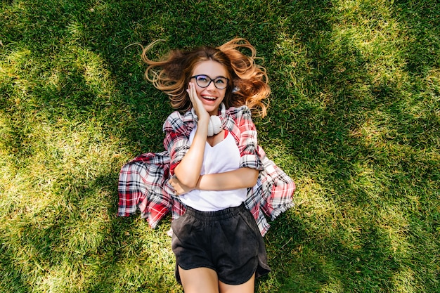 Wonderful pensive woman lying on soft green grass. overhead portrait of inspired european girl with happy face expression.