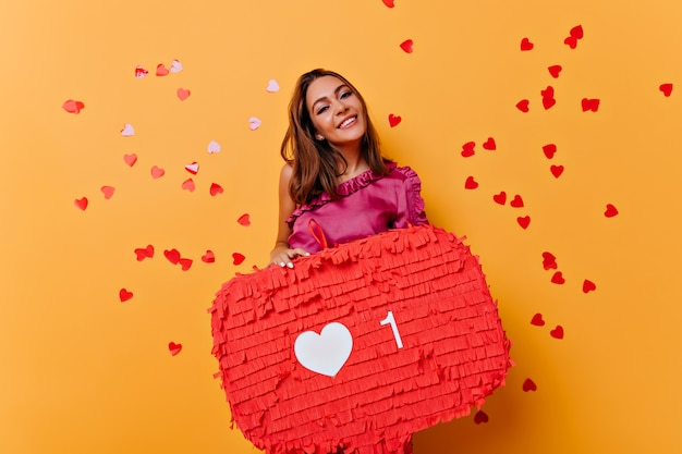 Wonderful smiling girl enjoying social networks. Indoor portrait of glamorous female blogger chilling on orange.