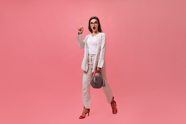 Wonderful woman in light suit walks on pink background.  Lady with red bright lips has cool idea and moves on isolated backdrop.