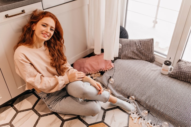 wonderful young lady with red hair smiling. indoor photo of glad caucasian girl sitting at home.