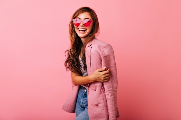 Foto gratuita meravigliosa giovane donna con i capelli lunghi che si diverte su roseo. magnifica ragazza in occhiali da sole alla moda rilassante durante il servizio di ritratti.