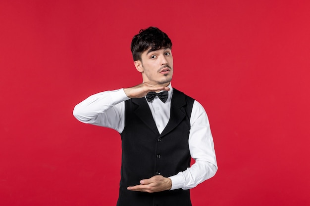 wondering male waiter in a uniform with butterfly on neck on red background