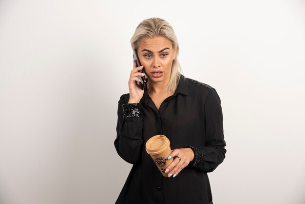 Wondering woman speaking on mobile phone and holding a cup of coffee . High quality photo