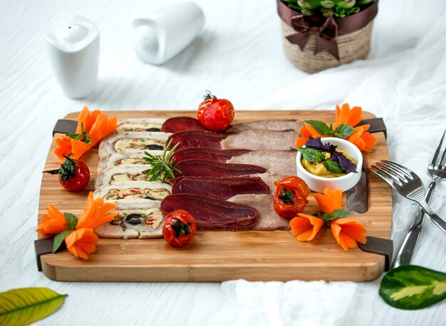 Wood board of meat side dishes garnished with sauce and vegetables