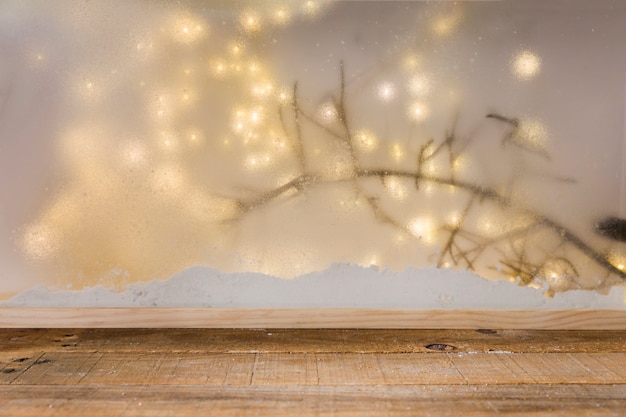 Wood table near bank of snow, plant twig and fairy lights