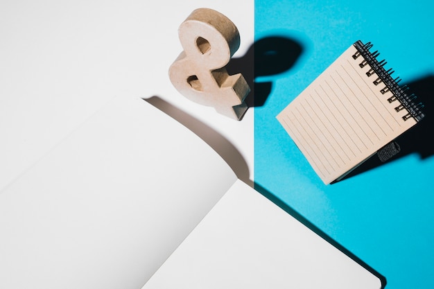 Wooden ampersand sign; spiral notepad and blank white page on dual wallpaper