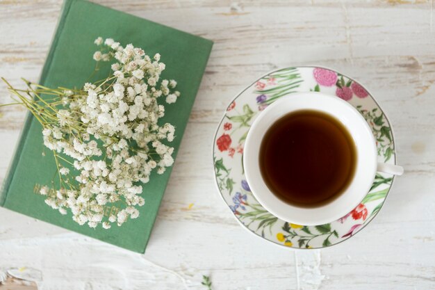 Wooden background with cup of tea, flowers and book