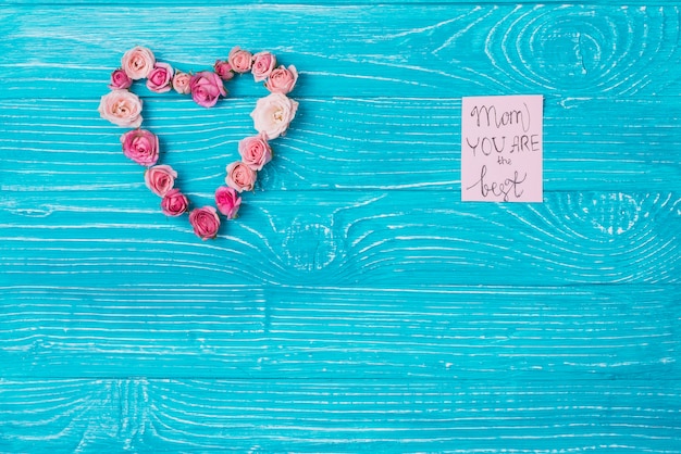 Wooden background with heart made of flowers and note for mother's day