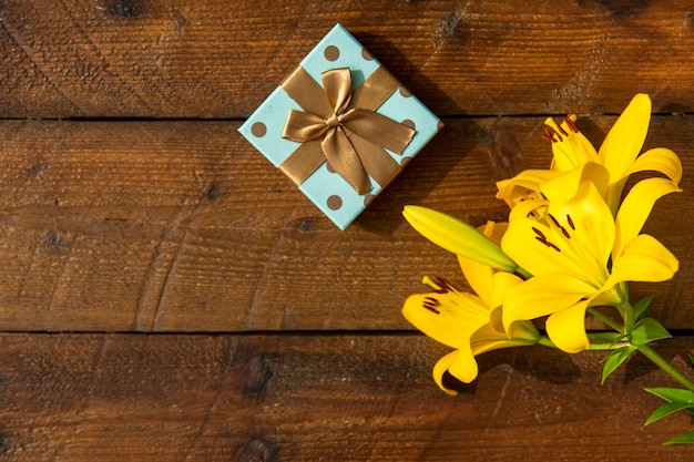 Wooden background with lilies and cute gift