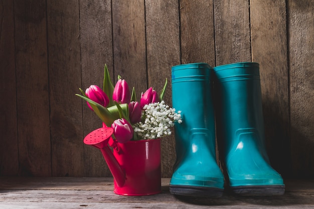 Wooden background with watering can and boots