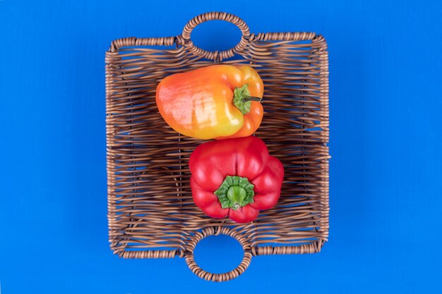 Wooden basket of colorful bell peppers on blue table.