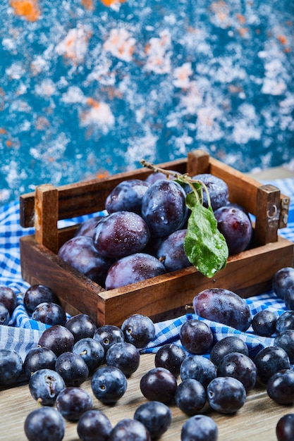 Wooden basket of fresh plums on blue.