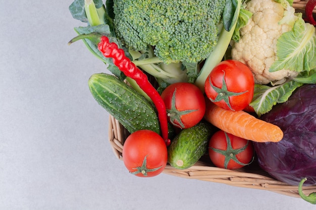 Wooden basket of fresh vegetables on white surface