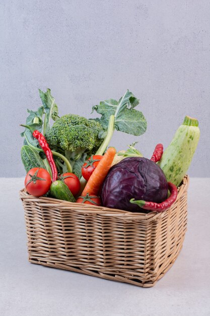 Wooden basket of fresh vegetables on white surface