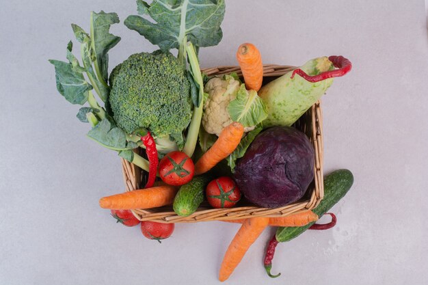 Wooden basket of fresh vegetables on white surface