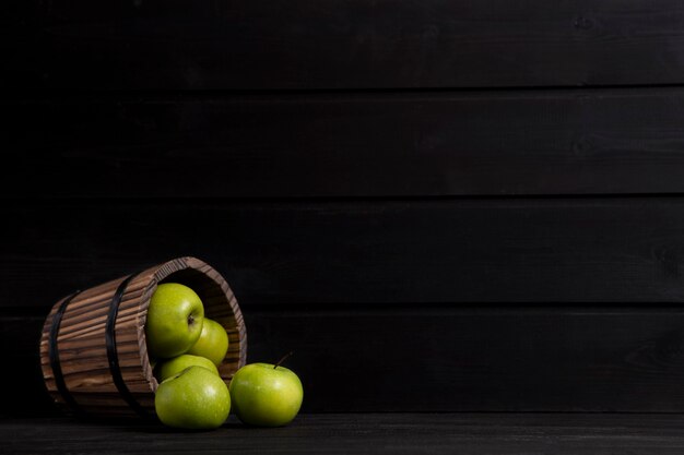 A wooden basket full of ripe green apples placed on a dark wooden table . High quality photo