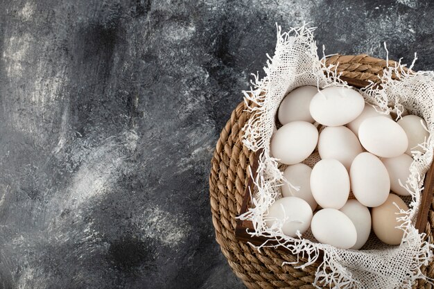 A wooden basket full of white raw chicken eggs . 