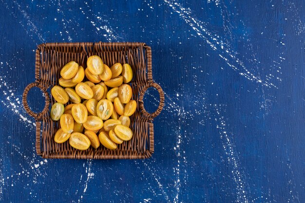 Free photo wooden basket of sliced kumquat fruits on marble surface.