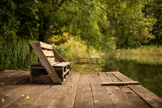 Деревянная скамейка на террасе на берегу озера в окружении зелени