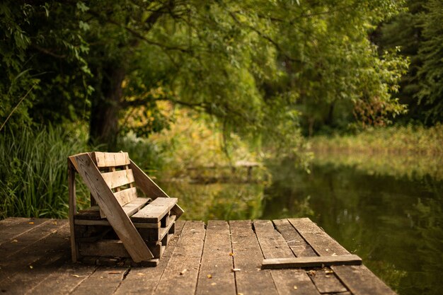 Wooden bench on the deck on the lake surrounded by greens