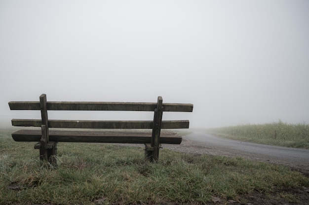 Wooden bench near the road covered with fog - solitude concept