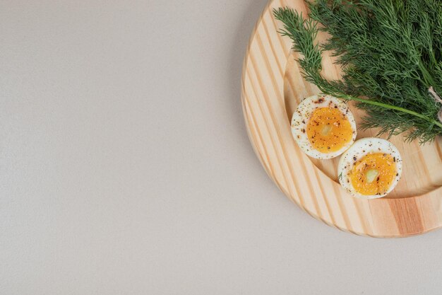 A wooden board of boiled egg with spices and greens .