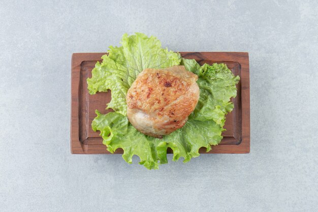 A wooden board of chicken fried meat with lettuce . 