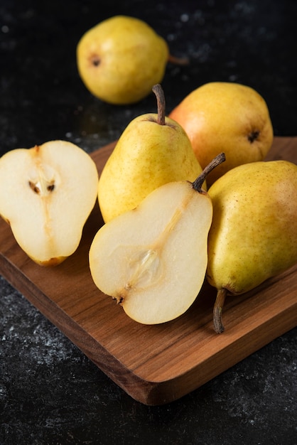 Tavola di legno di deliziose pere gialle su superficie nera.