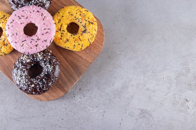 A wooden board of doughnuts with chocolate and yellow coating