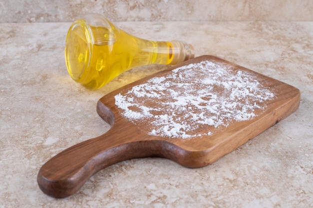 A wooden board of flour and a glass bottle of oil