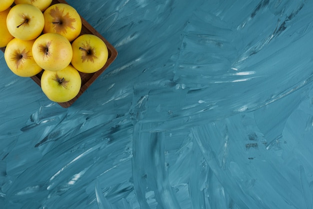 Wooden board of fresh yellow fruits on blue background.