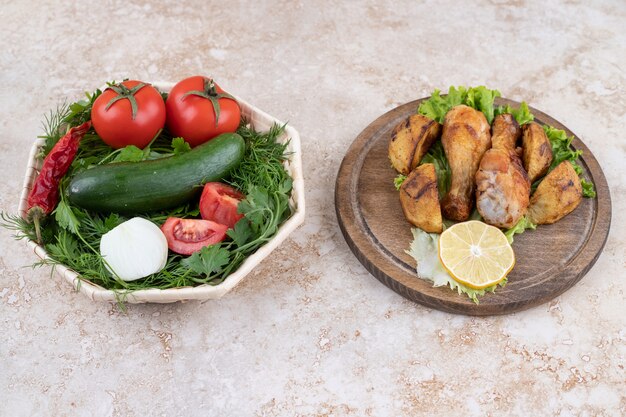 A wooden board of fried chicken legs meat and vegetables